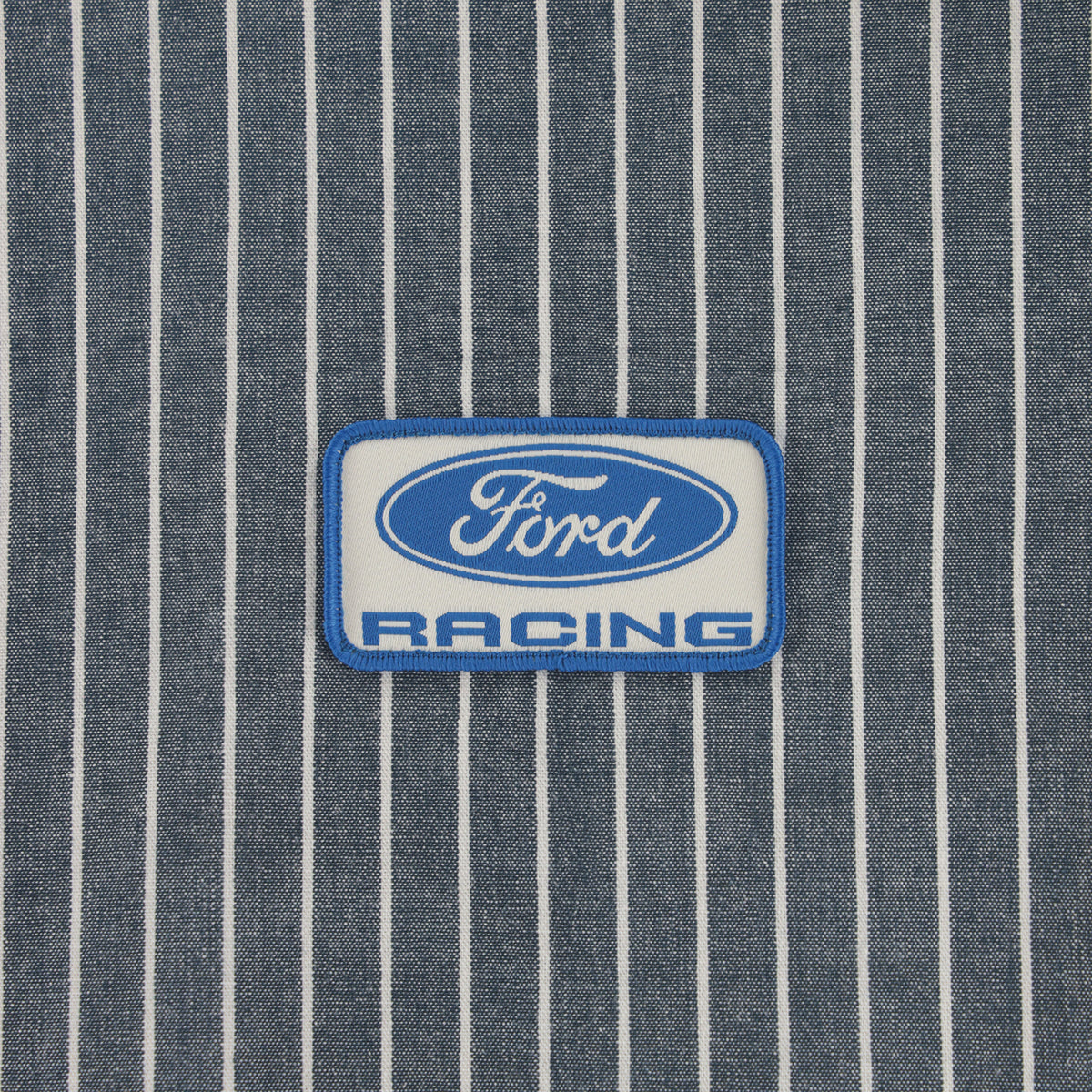 A rectangular embroidered patch with the Ford Racing logo, featuring a blue and white design, placed on a blue and white pinstriped fabric background.