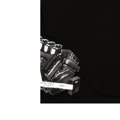A close-up of a black garment, likely a t-shirt, featuring a detailed black and white graphic print of a V8 engine block with chrome valve covers and a white distressed label overlay.