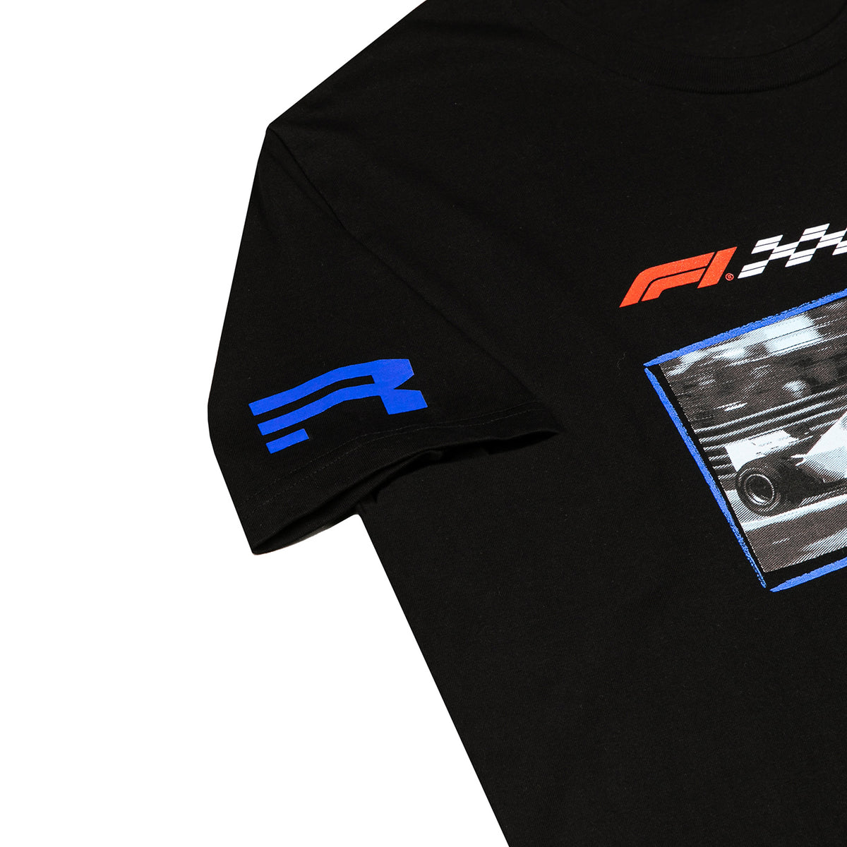 Close-up of a black short-sleeve T-shirt showing the right sleeve with a blue stylized logo, part of the chest graphic with an orange and white F1-style mark, and a rectangular racing-themed print.