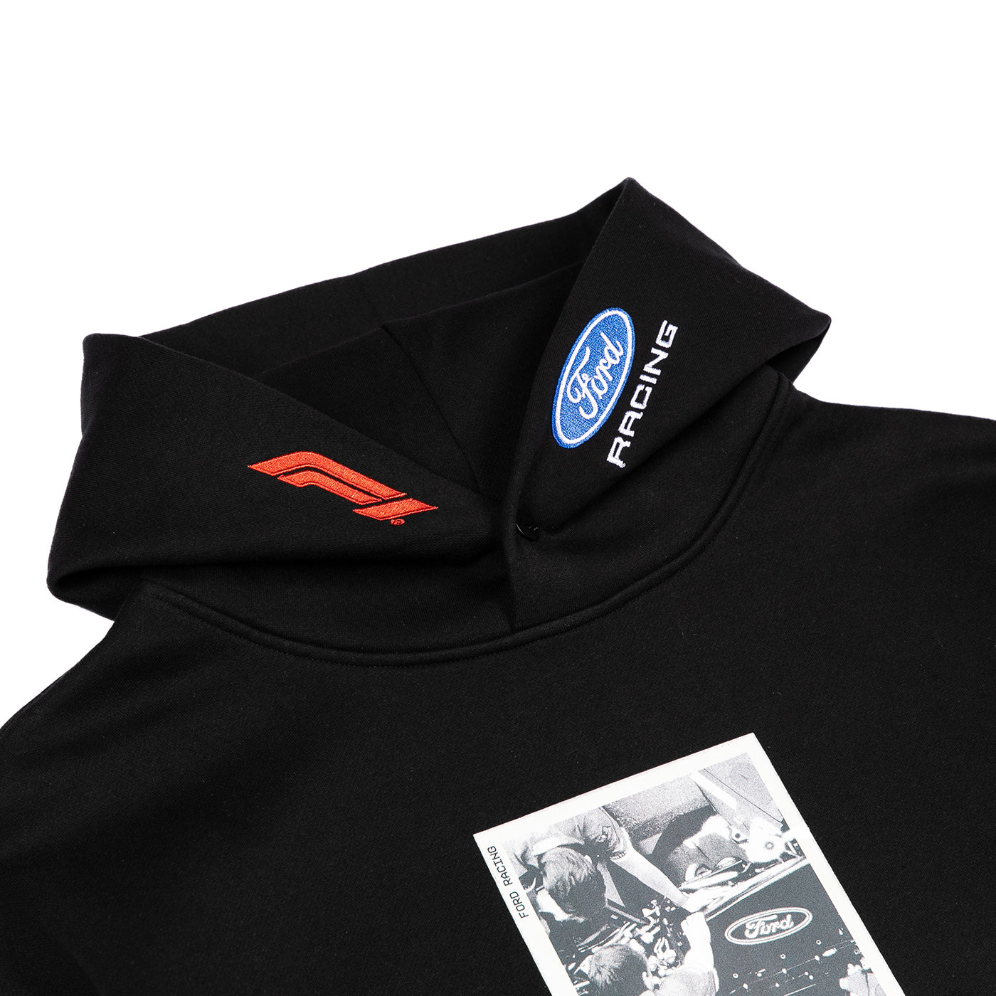 Close-up of a black Ford Racing hoodie showing the inner collar with a blue oval Ford Racing logo and white 'RACING' text, plus a red embroidered logo on the opposite shoulder and a black-and-white printed graphic on the chest.
