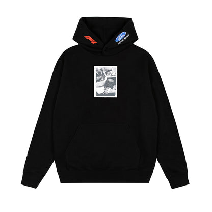A black pullover hoodie with a kangaroo pocket, featuring a rectangular black-and-white graphic print on the chest and small red and blue logo patches on the hood.