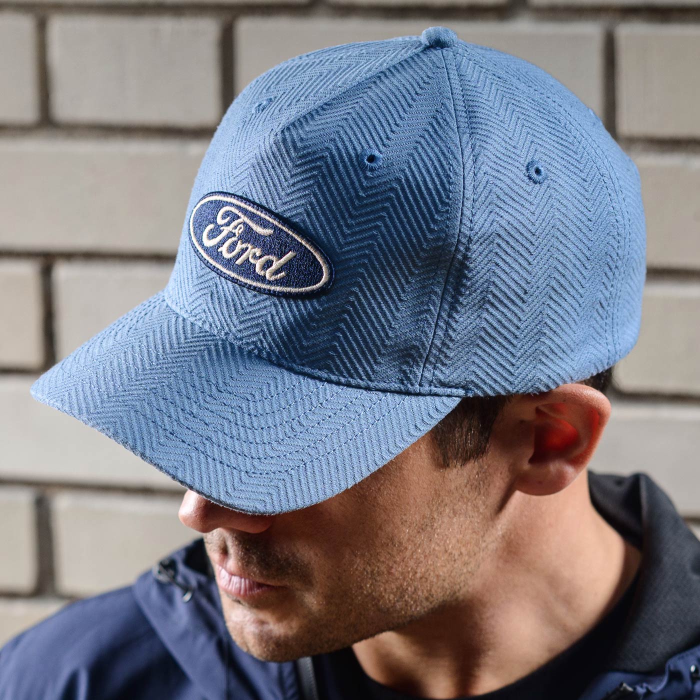 Person wearing a blue cap with a Ford logo against a brick wall.