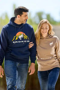 Two people wearing Bronco hoodies walking outdoors with a blurred natural background