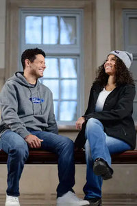 Two people sitting on a bench with a Ford hoodie and jacket in an indoor setting.
