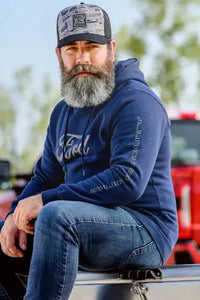 Man with a beard wearing a blue Ford Truck Super Duty hoodie and cap, sitting on a vehicle.