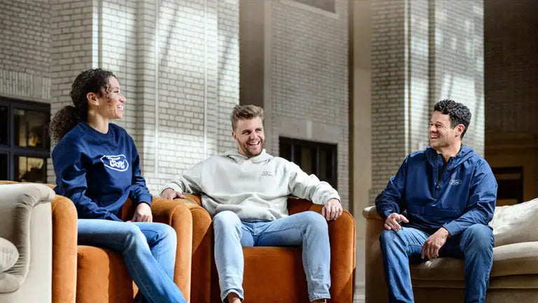 Three people sitting on a couch wearing Ford merchandise apparel in a modern indoor setting