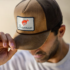 Man wearing a brown cap with a 'Bronco' logo against a blurred background