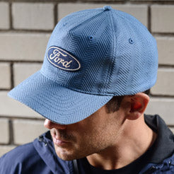 Person wearing a blue Ford oval hat  against a brick wall.