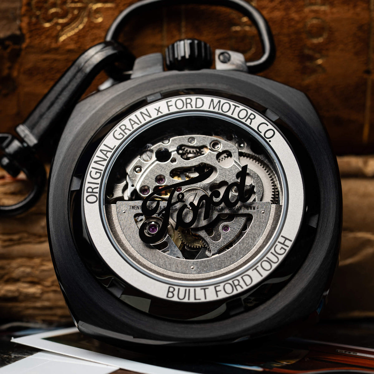 Close-up of a mechanical watch with 'Original Grain x Ford Motor Co' branding on a wooden background.