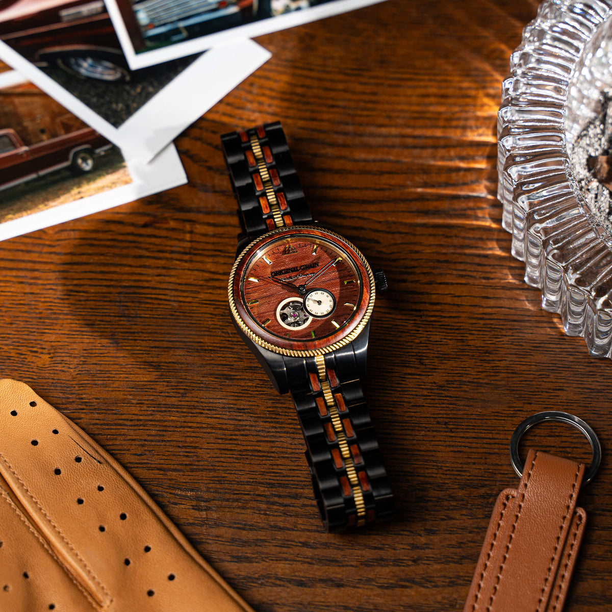 Wooden watch with black and gold accents on a wooden surface with a leather case and glass container.