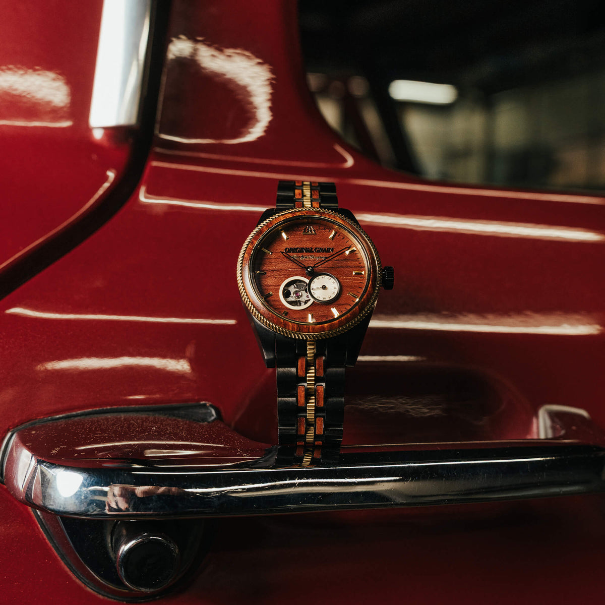 Luxury watch with wooden face and brown strap on a red car door handle